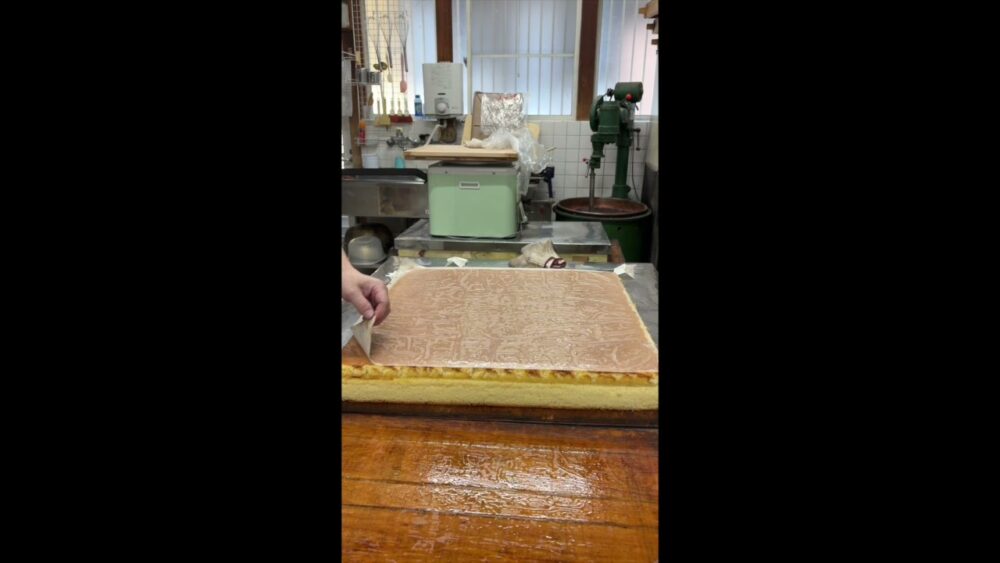 焼き上がったカステラに包丁を入れる職人の手
